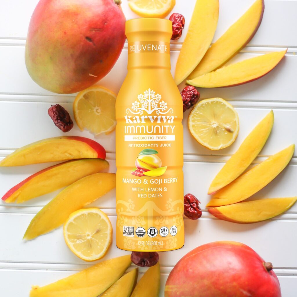 A bottle of Karviva Immunity Mango and Goji berry, surrounded by mango slices, lemon halves, and whole goji berries.