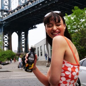 Woman holding beverage under city bridge