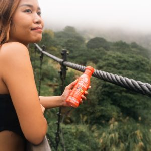 Woman holding orange detox drink overlooking lush valley
