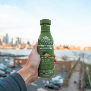 Hand holding green detox juice bottle outdoors